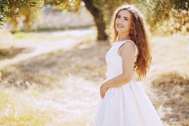 Schöne langhaarige Braut in einem ausgezeichneten weißen Kleid, das in Natur geht