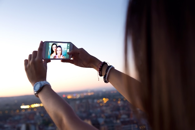 Kostenloses Foto schöne mädchen, die ein selfie auf dem dach bei sonnenuntergang.