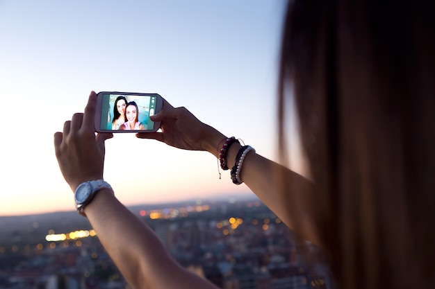 Schöne Mädchen, die ein Selfie auf dem Dach bei Sonnenuntergang.