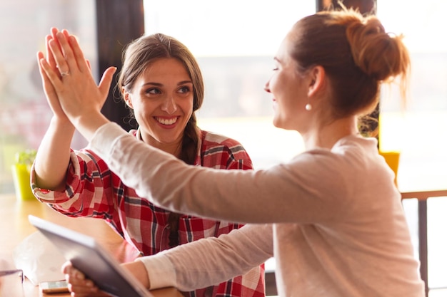 Kostenloses Foto schöne mädchen, die highfive geben, während sie ihre freizeit im café verbringen und über alltägliche dinge sprechen.