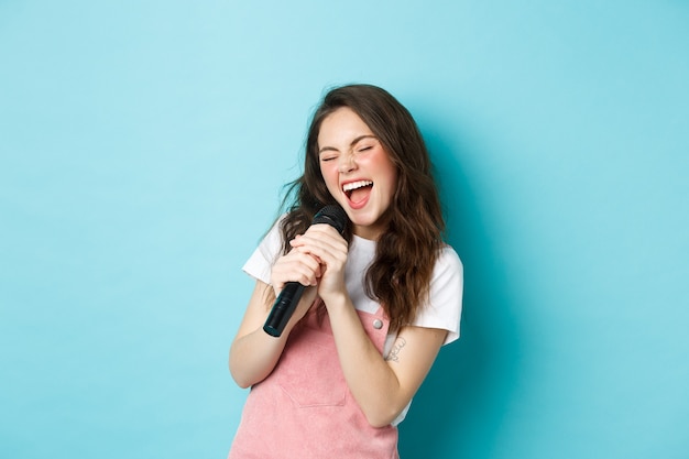 Schöne Mädchensängerin, die Mikrofon hält, Karaoke im Mikrofon singt und auf blauem Hintergrund steht.