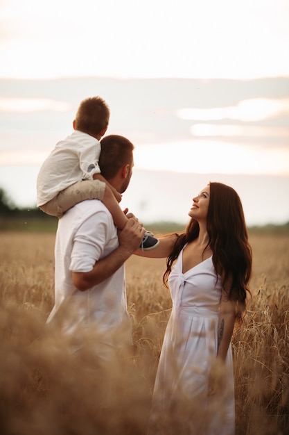 Schöne Mama, Papa und ihr süßes kleines Kind haben Spaß zusammen und lächeln draußen