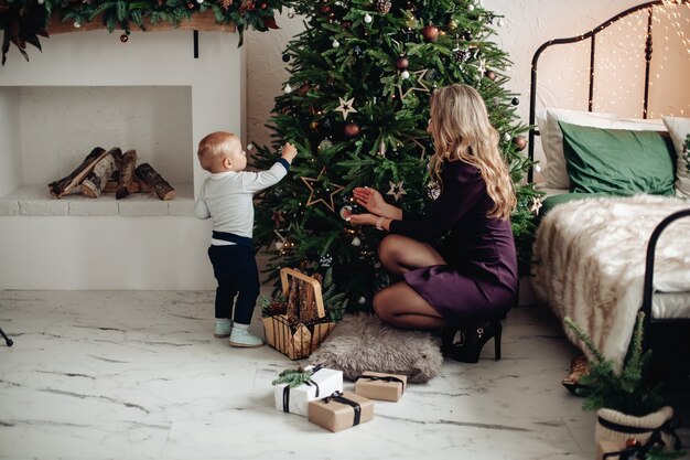 Schöne Mutter hilft ihrem kleinen Sohn, einen Weihnachtsbaum zu schmücken