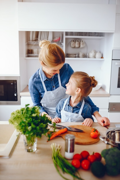 schöne Mutter in einem blauen Hemd und in der Schürze bereitet einen Frischgemüsesalat zu Hause vor