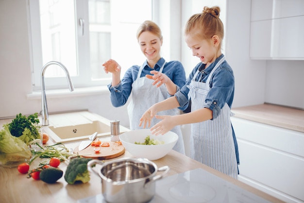 schöne Mutter in einem blauen Hemd und in der Schürze bereitet einen Frischgemüsesalat zu Hause vor