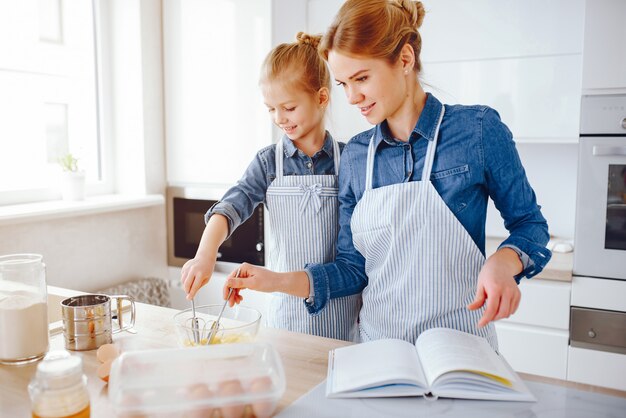 schöne Mutter in einem blauen Hemd und Schürze bereitet Abendessen zu Hause in der Küche vor