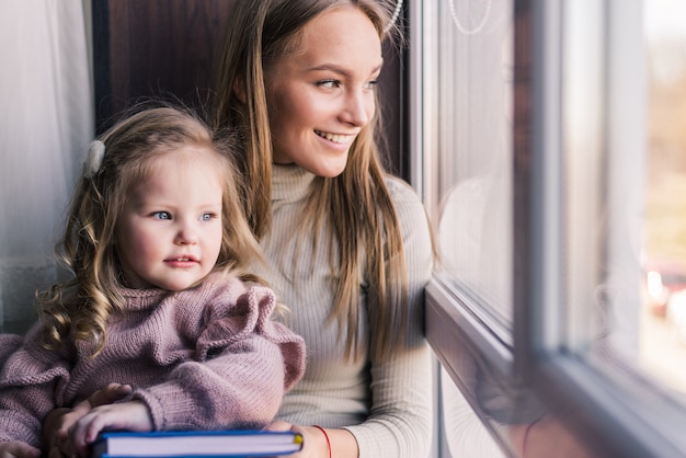 Kostenloses Foto schöne mutter mit tochter. familie, die im raum nahe fenster sitzt und nach draußen schaut