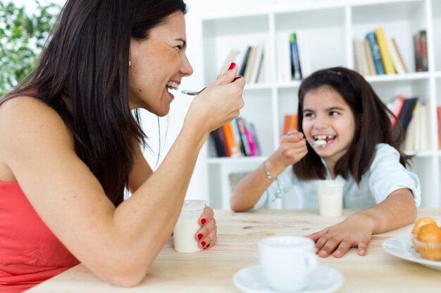 Schöne Mutter und ihre Tochter essen Joghurt zu Hause.
