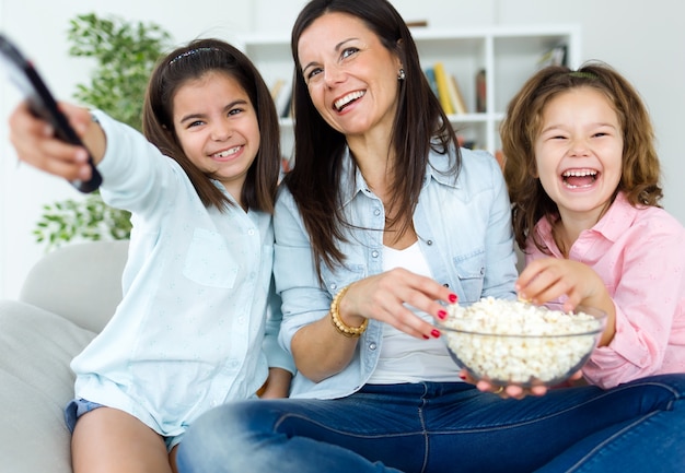 Schöne Mutter und ihre Töchter essen Popcorns zu Hause.