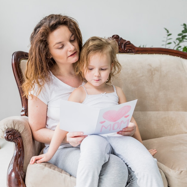 Schöne Mutter- und Tochterlesetagesgrußkarte des Muttertags, die auf Sofa sitzt