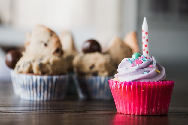 Schöne Nahaufnahme eines leckeren rosa Cupcakes gegen Schokoladencupcakes auf einem Holztisch