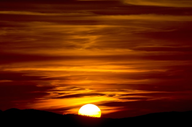 Schöne Nahaufnahmeaufnahme eines Sonnenuntergangs mit gelesenem Himmel und halber Sonne in der Toskana, Italien