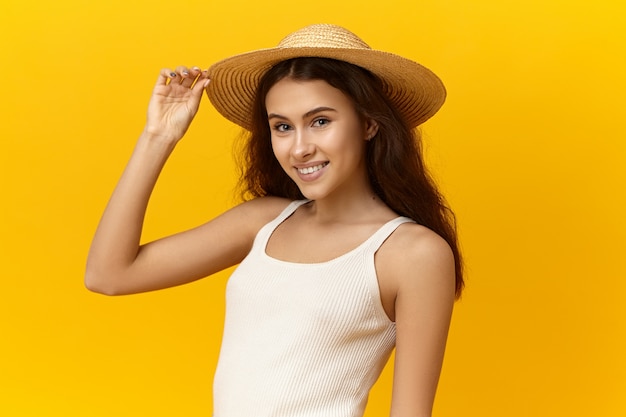 Schöne romantische junge Frau, die Strohhut und weißes Trägershirt trägt und Sommerferien genießt