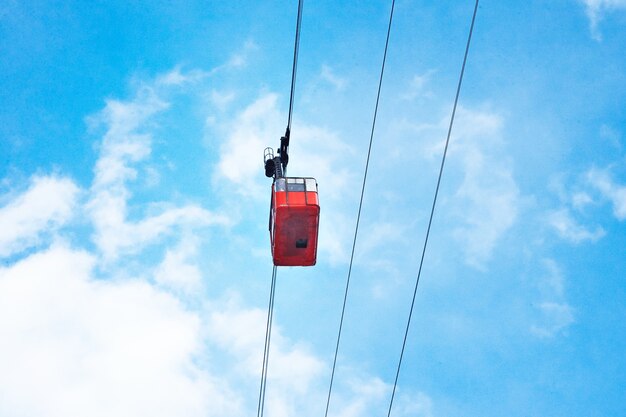 Schöne rote Luftzugbahnkabine der Weinlese, die über, lokalisiert auf hellblauem Himmel bewegt