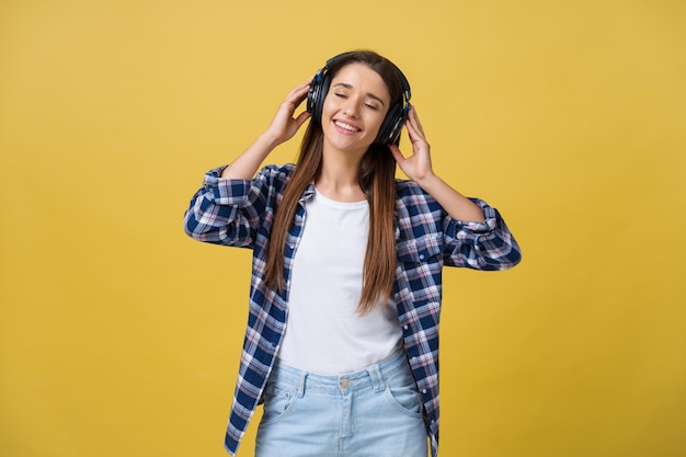 Schöne ruhige junge Frau, die die Musik im Kopfhörer mit geschlossenen Augen auf gelbem Hintergrund hört Nahaufnahme