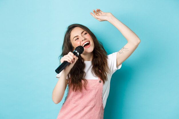 Schöne Sängerin, die Mikrofon hält, Karaoke im Mikrofon singt und auf blauem Hintergrund steht