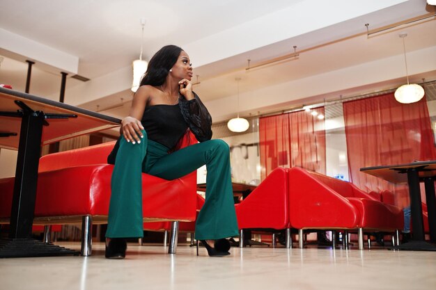 Schöne schlanke afroamerikanische Modelabnutzung auf schwarzer Bluse und grüner Hose mit langen Beinen posierte im chinesischen Café