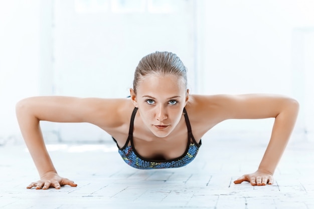 Schöne schlanke Brünette, die einige Liegestütze im Fitnessstudio macht