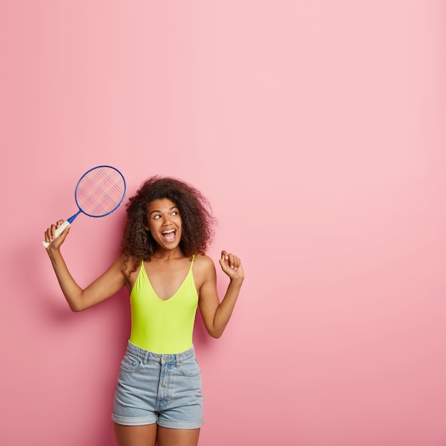 Schöne schlanke sorglose dunkelhäutige Frau spielt Badminton oder Tennis, hält Schläger