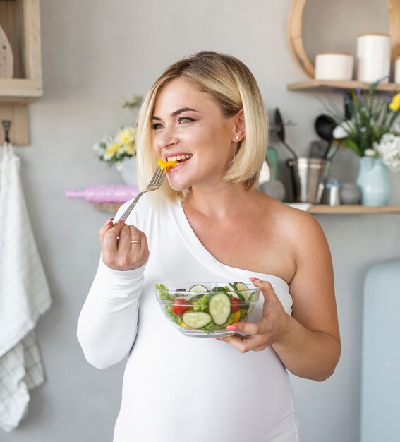 Schöne schwangere Frau der Vorderansicht, die Salat isst