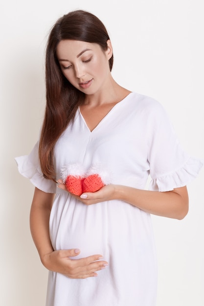 Schöne schwangere Frau mit roten Babyschuhen lokalisiert