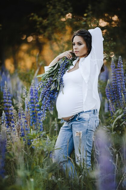 Schöne schwangere Frau steht mit Lupinusstrauß unter Rasen