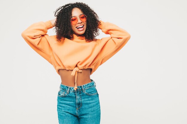 Schöne schwarze Frau mit Afrolockenfrisur. Lächelndes Model in orangefarbenem Hoodie und trendiger Jeanskleidung