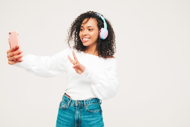 Schöne schwarze Frau mit Afrolockenfrisur. Lächelndes Modell in Pullover und Jeans