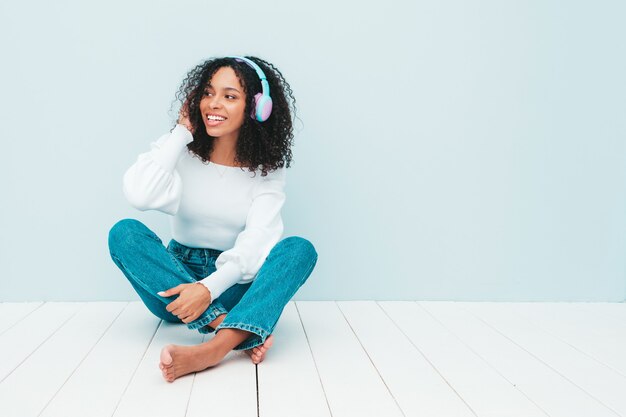 Schöne schwarze Frau mit Afrolockenfrisur. Lächelndes Modell in Pullover und Jeans