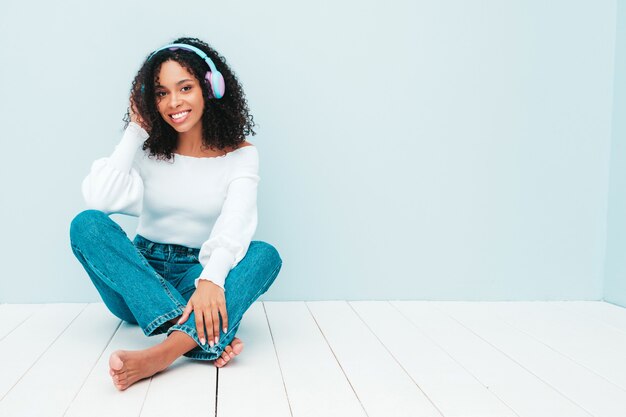 Schöne schwarze Frau mit Afrolockenfrisur. Lächelndes Modell in Pullover und Jeans
