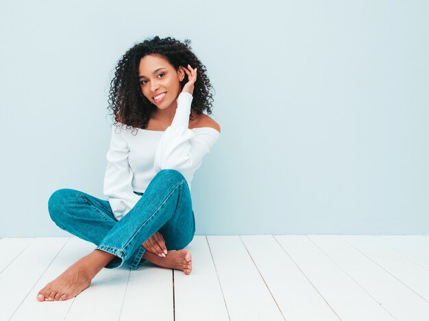 Schöne schwarze Frau mit Afrolockenfrisur. Lächelndes Modell in Pullover und trendiger Jeanskleidung