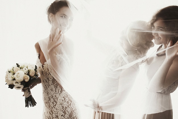 Schöne sexuelle Brünette Braut in weißen Kleid mit Brautjungfern in der Nähe von Fenster