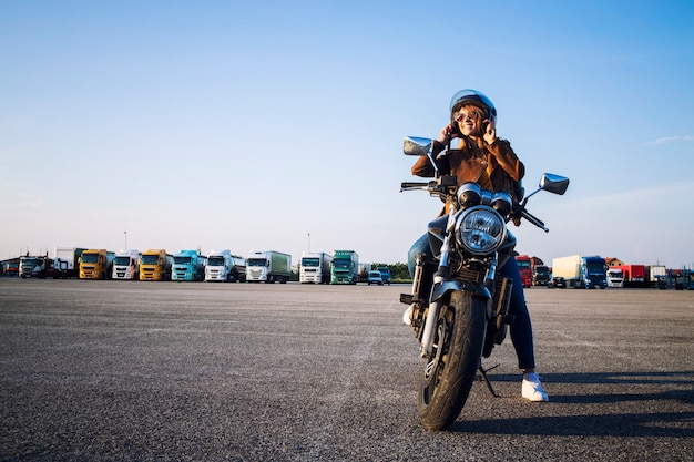Schöne sexy brünette Frau in der Lederjacke, die auf Retro-Artmotorrad sitzt und sich auf die Fahrt vorbereitet