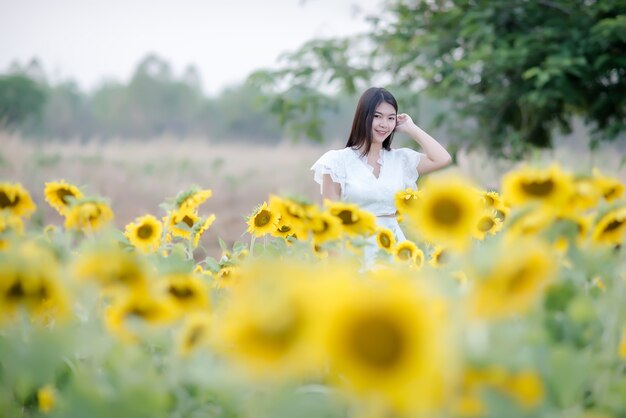 schöne sexy Frau in einem weißen Kleid zu Fuß auf einem Feld von Sonnenblumen