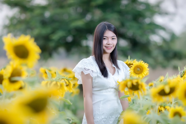 schöne sexy Frau in einem weißen Kleid zu Fuß auf einem Feld von Sonnenblumen