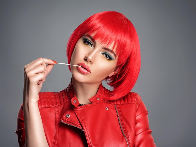 Schöne sexy Frau mit leuchtend roter Bob-Frisur. Model. Sinnlich schönes Mädchen in einer Lederjacke. Atemberaubendes Gesicht einer hübschen Dame. Helles Mädchen streckt Kaugummi