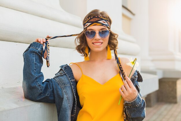 Schöne sexy stilvolle Frau im gelben stilvollen Kleid, das Jeansjacke, trendiges Outfit, Frühlingssommer-Modetrend, sonnige, blaue Sonnenbrille, Straßenmode, Hipster-Stil, modische Accessoires trägt