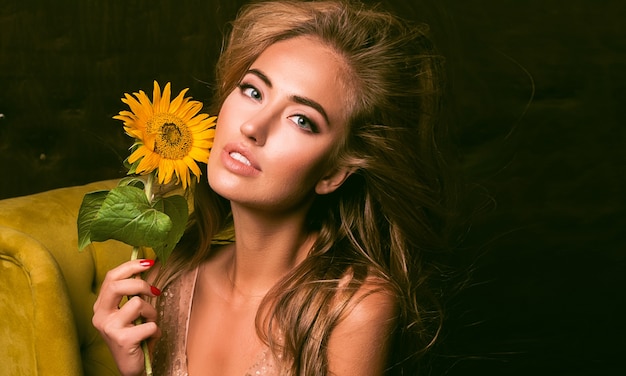 Kostenloses Foto schöne sinnliche frau, die auf dem sessel sitzt und mit sonnenblume aufwirft