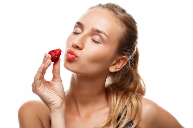 Schöne sportliche Frau, die aufwirft, Erdbeere isst