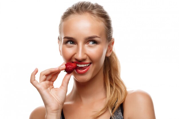 Schöne sportliche Frau, die aufwirft, Erdbeere isst
