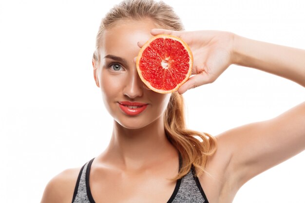 Schöne sportliche Frau, die aufwirft, Grapefruit hält
