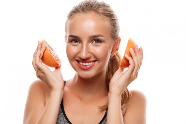 Schöne sportliche Frau, die aufwirft, Grapefruit hält