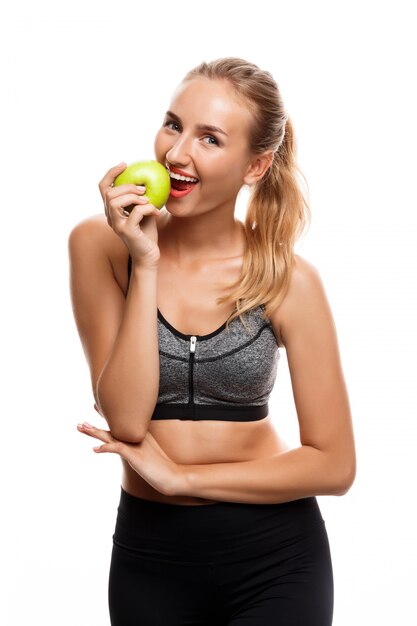Schöne sportliche Frau, die aufwirft und Apfel hält