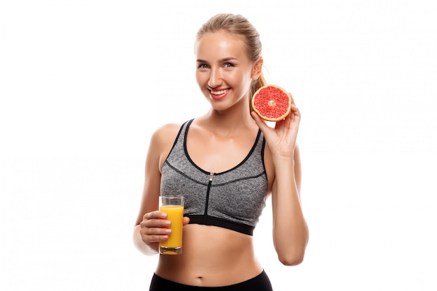 Schöne sportliche Frau, die Grapefruit und Saft hält