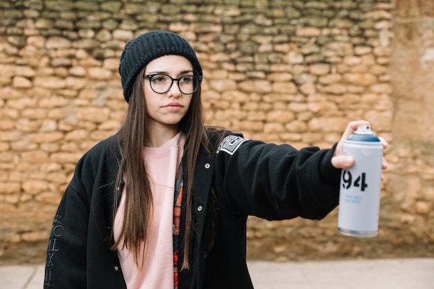 Schöne Sprühdose der jungen Frau, die vor Steinwand steht