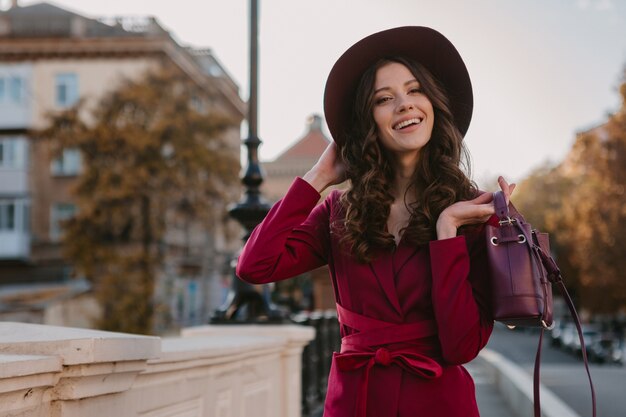 Schöne stilvolle Frau im lila Anzug, der in Stadtstraße, Frühlingssommer-Herbstsaison-Modetrend trägt Hut trägt und Geldbörse hält