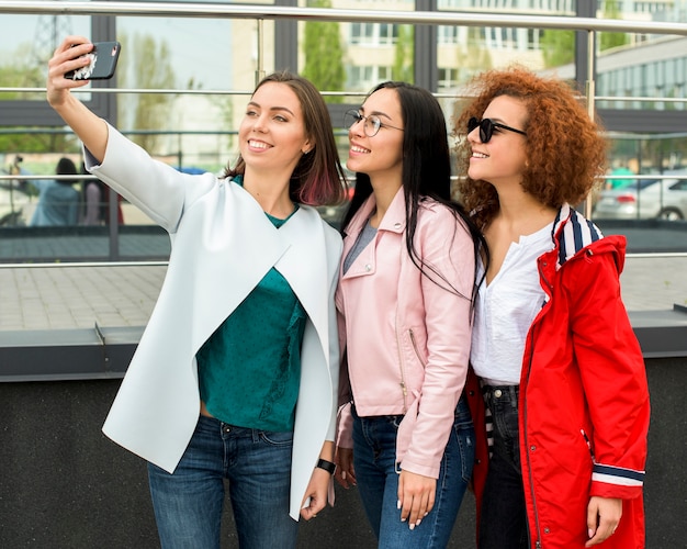 Kostenloses Foto schöne stilvolle freundinnen, die selfie im smartphone nehmen