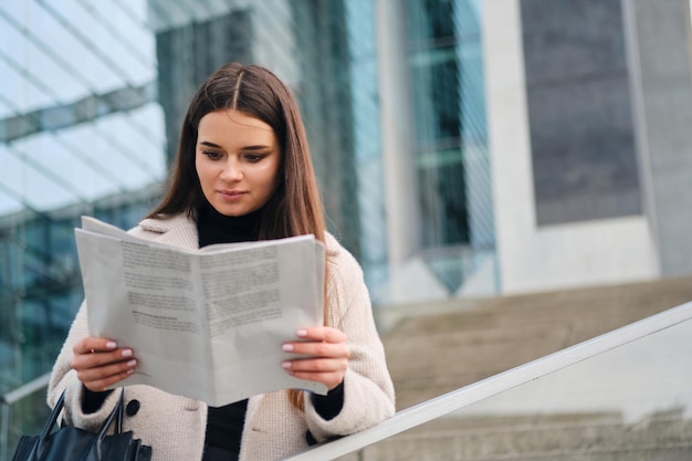 Schöne stilvolle Geschäftsfrau, die nachdenklich Zeitung im Stadtzentrum liest