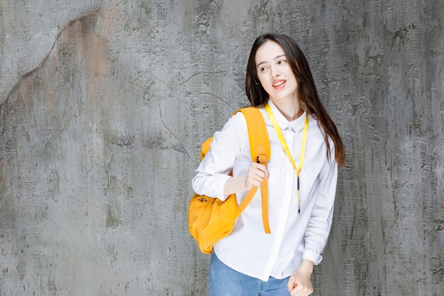 Schöne Studentin mit gelber Rucksackstellung. Foto in hoher Qualität