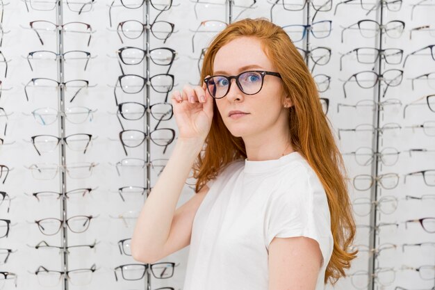 Schöne tragende Brillen der jungen Frau, die Kamera im Optikershop betrachten